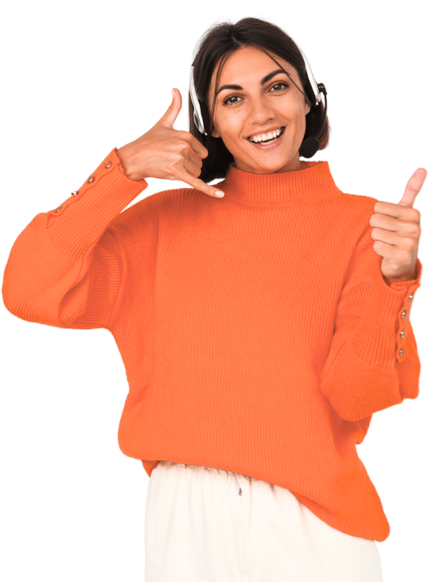 Smiling woman wearing an orange sweater and white pants, with headphones on, making a call gesture and giving a thumbs up.