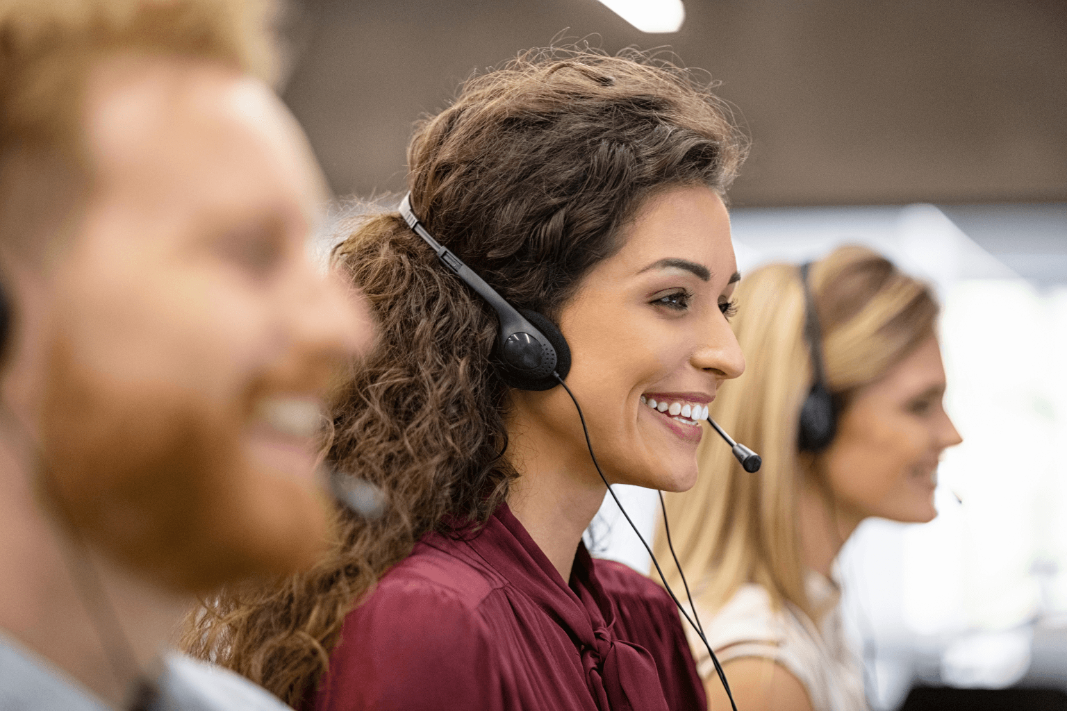 Three customer service agents wearing headsets and smiling in an office.