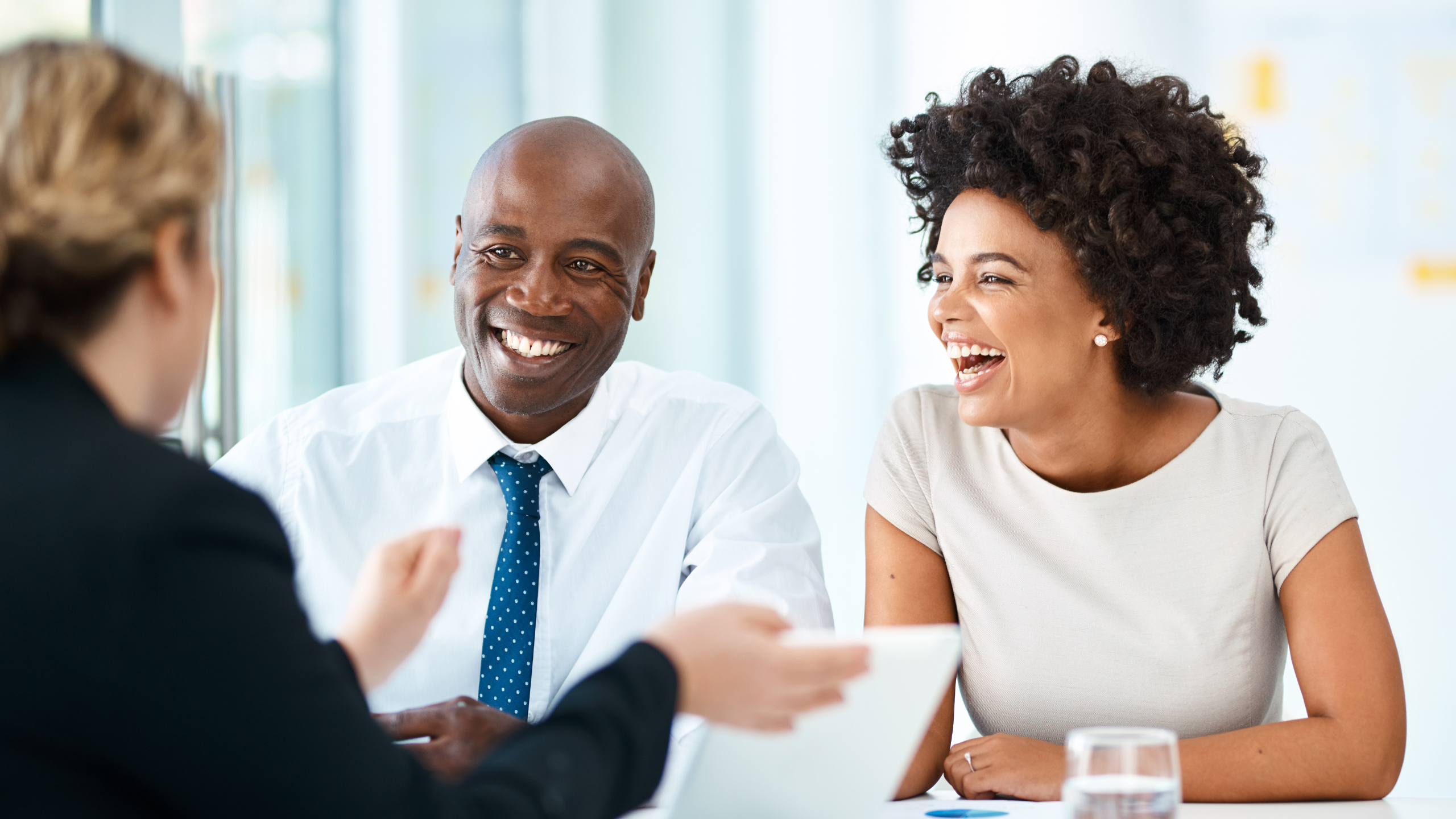 Three colleagues in a bright office share a friendly conversation during a meeting.