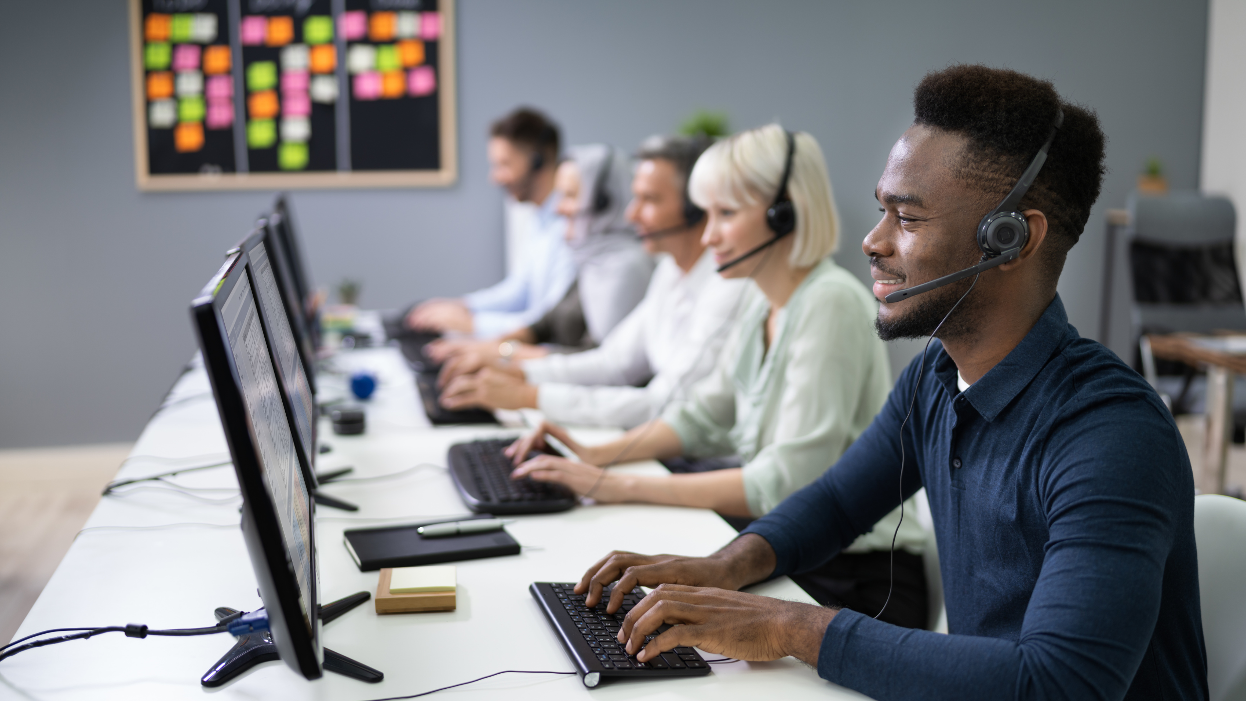 A group of call center agents wearing headsets work at their computers in a modern office.