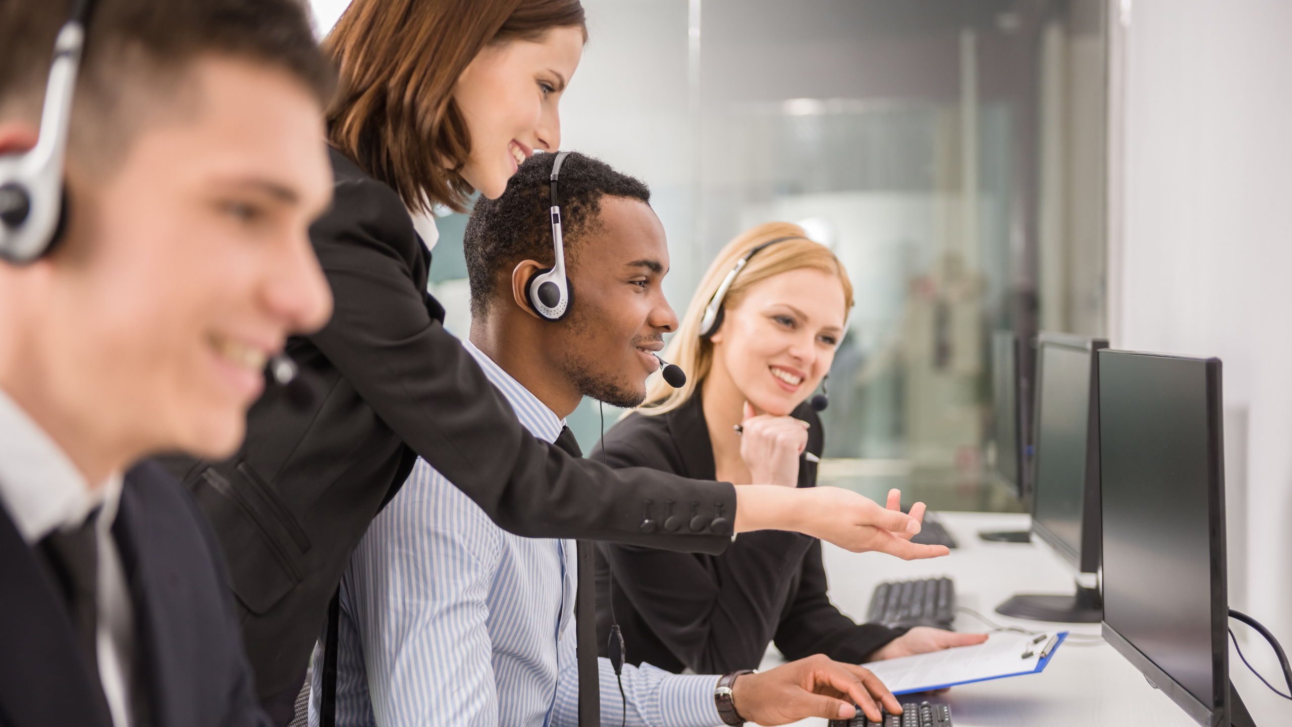 A diverse team of customer service agents wearing headsets work at computers in a bright office.