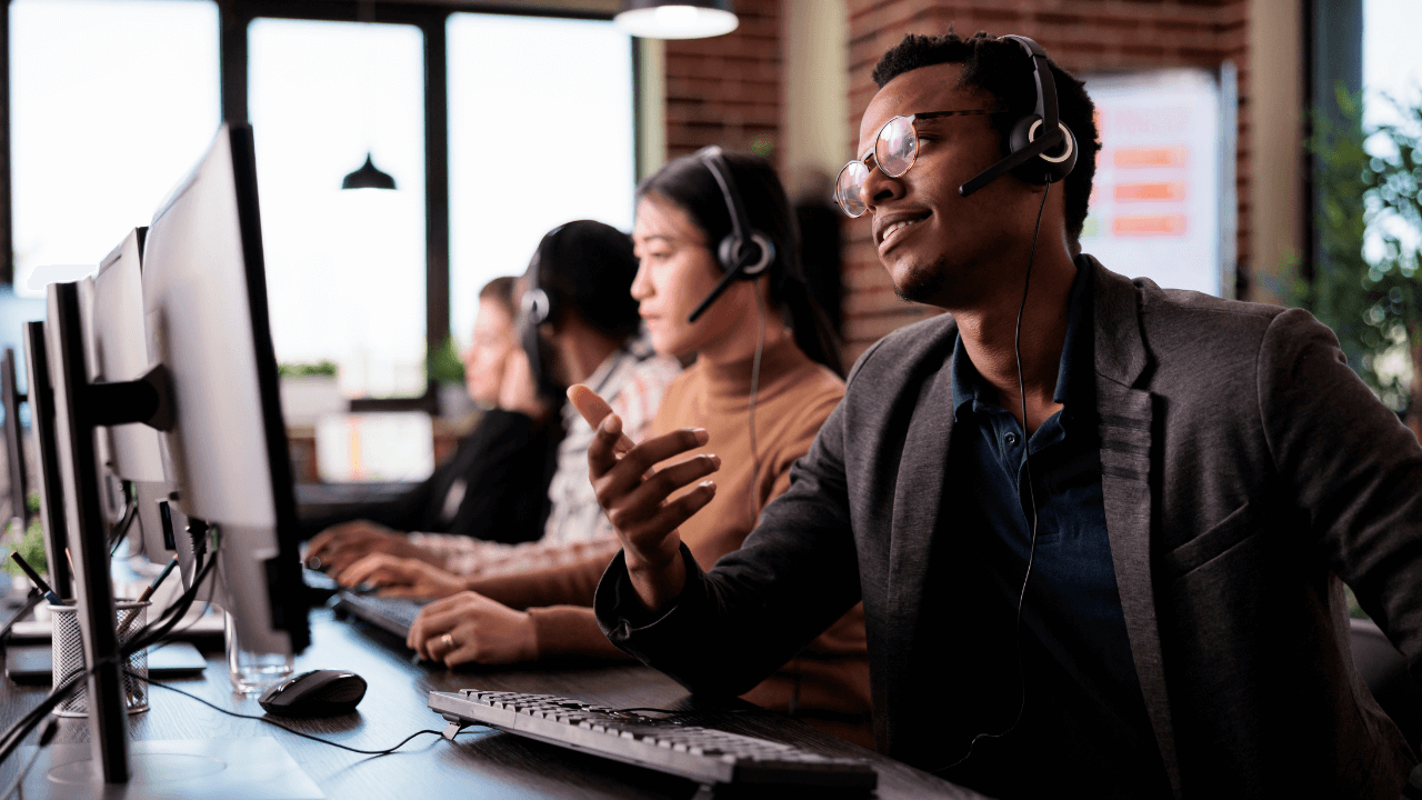 A group of customer service agents wearing headsets work at computer stations in a call center.
