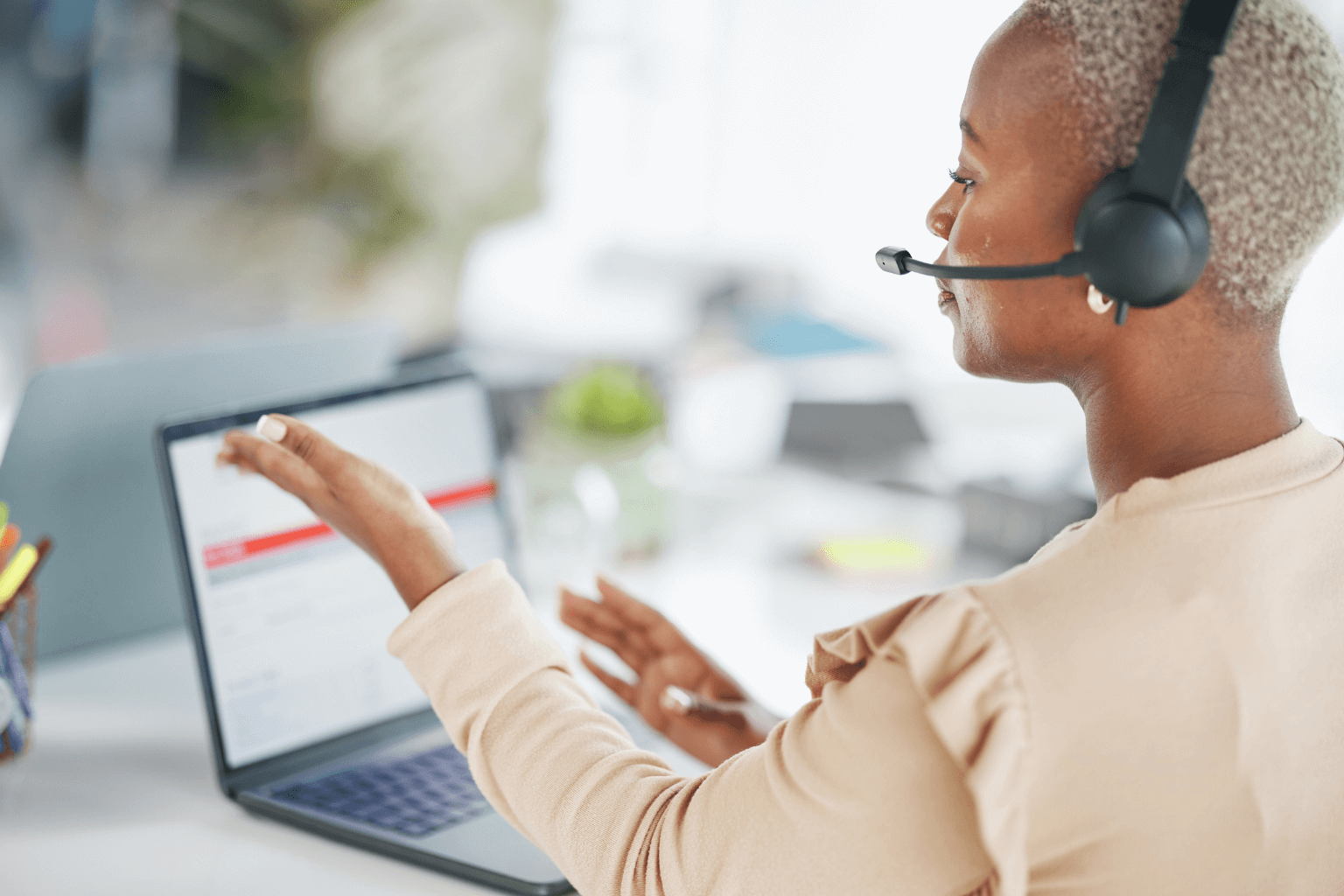A person wearing a headset and using a laptop at a desk in an office.